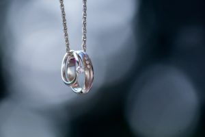 A silver engagement ring and wedding band set with diamonds on a silver chain.